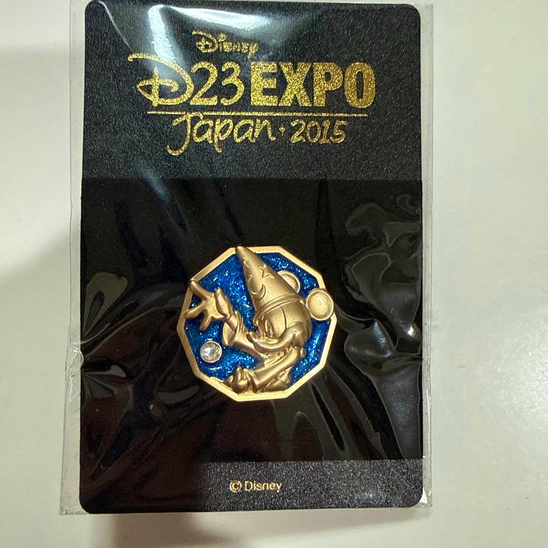 Front view of the D23 Expo Japan 2015 pin badge on its black backing card showing a gold-colored octagonal pin with a blue glitter background.