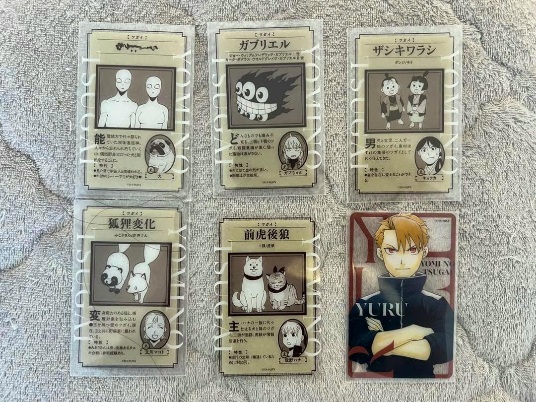 Six clear plastic cards from the set arranged on a towel, five with monochrome character/creature illustrations and one with a colored character portrait.