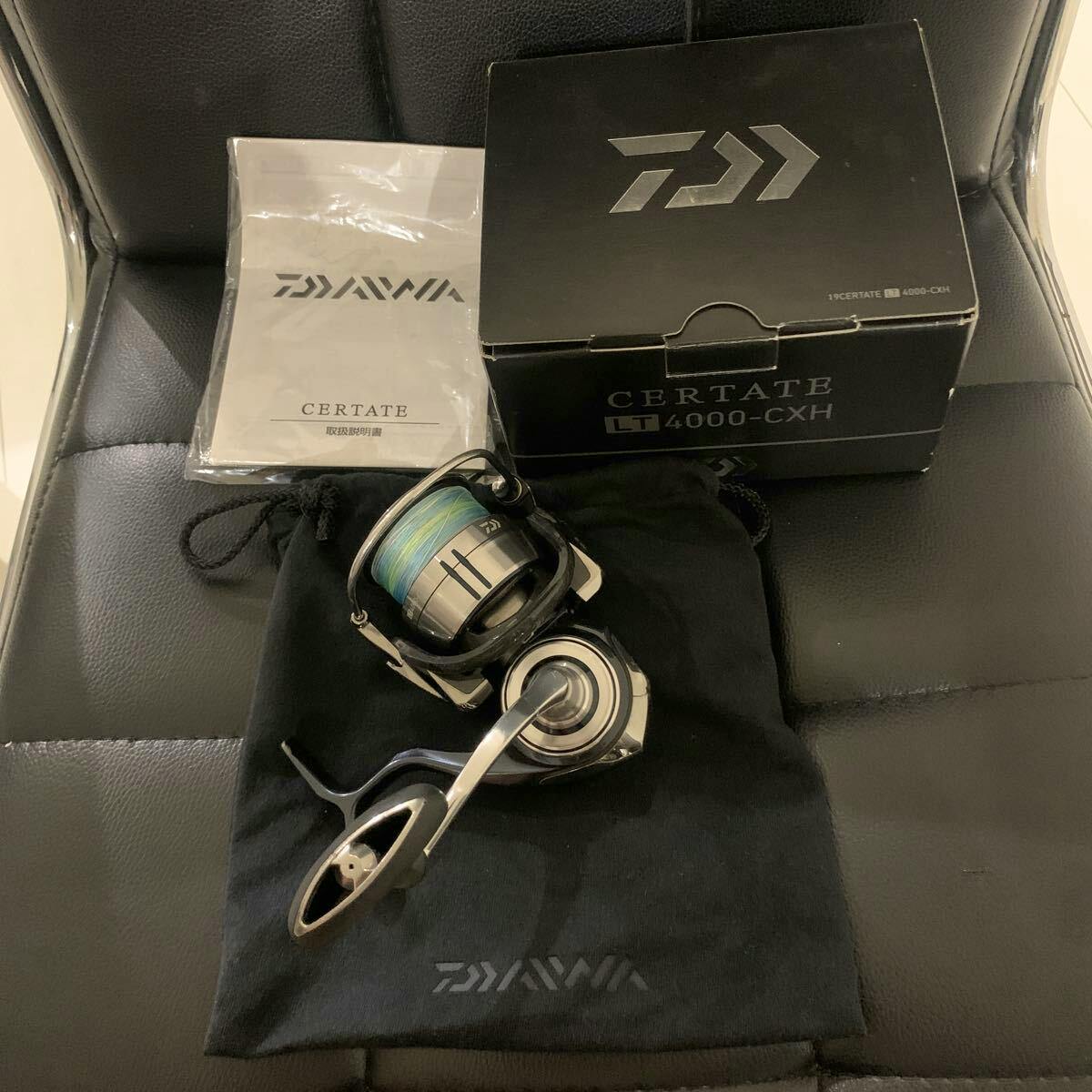 DAIWA Certate LT4000-CXH fishing reel shown with its box, instruction manual, and a black pouch on a chair.