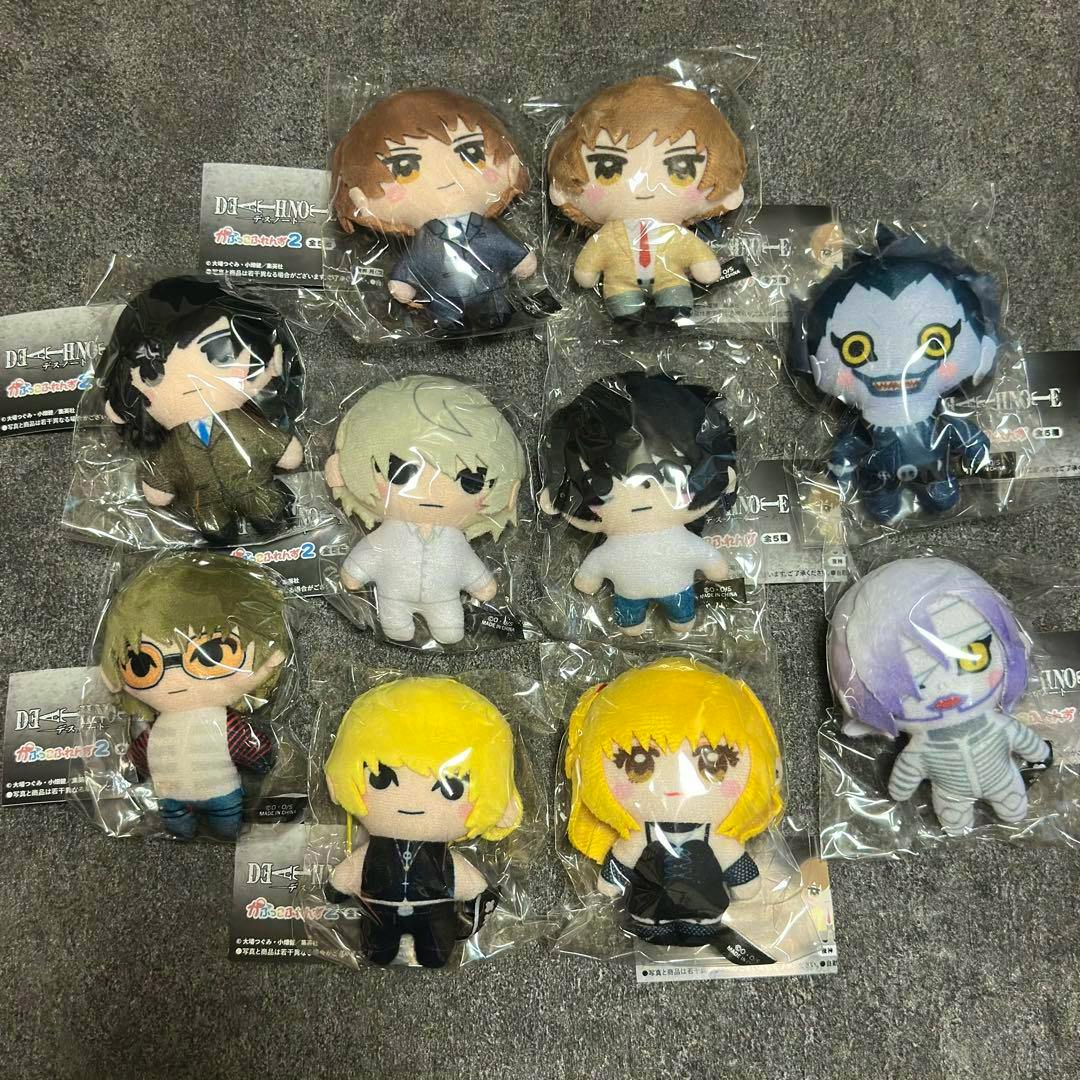 Photo of multiple Death Note character plush toys in their plastic packaging arranged on a gray surface.