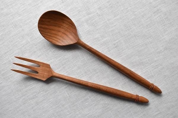 A decorative wooden fork and spoon lying on a light fabric background.