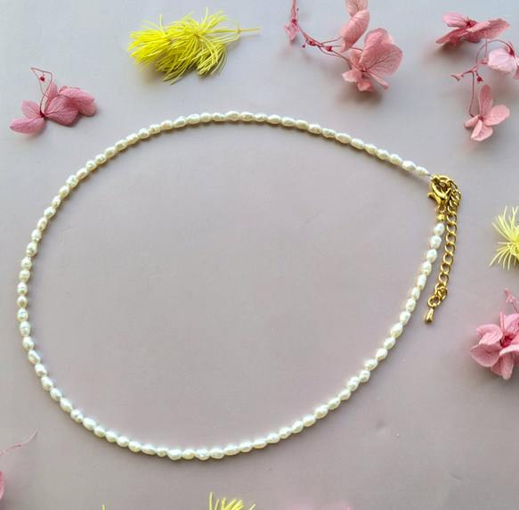 A single-strand necklace of small white beads arranged on a pink background with scattered flowers.