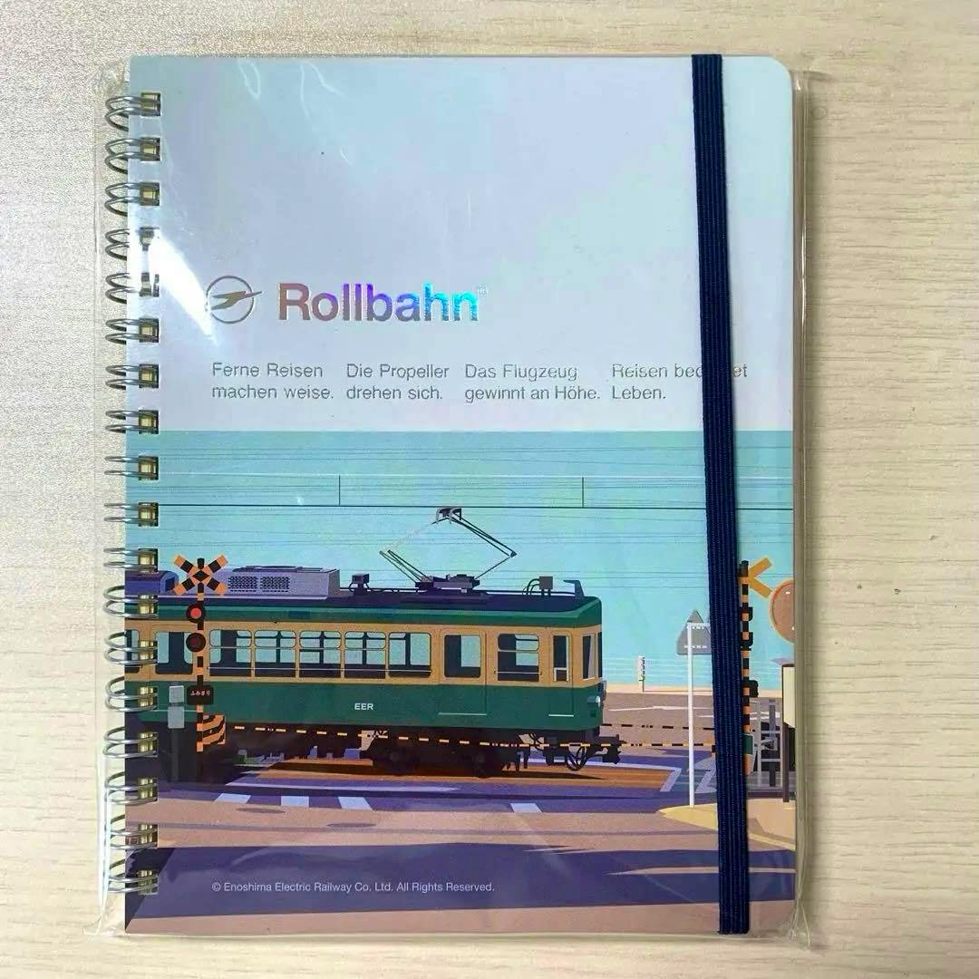 Spiral-bound Rollbahn pocket notebook in plastic wrap showing an Enoden train crossing illustration on the cover with a navy elastic band.