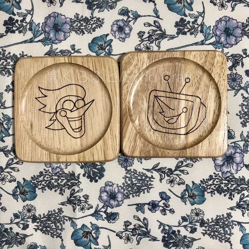 Two square wooden coasters with recessed circular wells and engraved Deltarune character faces on floral fabric.