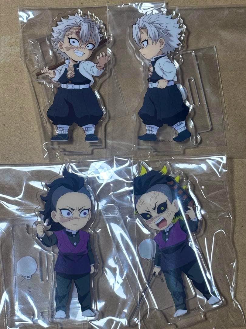 Four acrylic Demon Slayer character standees (Shinazugawa brothers) in their plastic packaging laid on a flat surface.