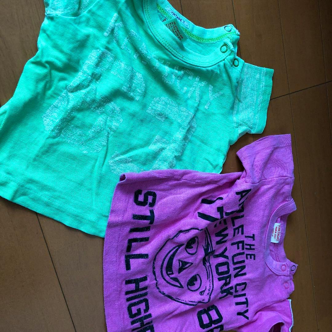 Two children's cotton shirts (green and purple) laid flat on a wooden floor.