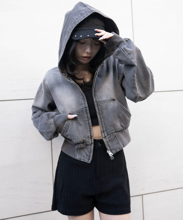 Woman wearing the denim short hooded jacket, shown front view with hood up and hands in the pockets.