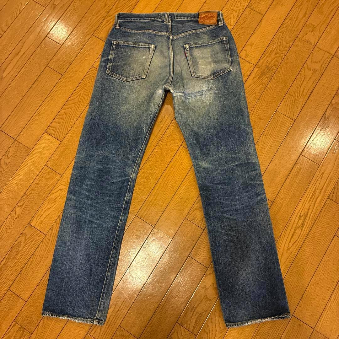 Back view of DENIME men's denim jeans (34-inch) laid flat on a wooden floor, showing rear pockets and straight legs.