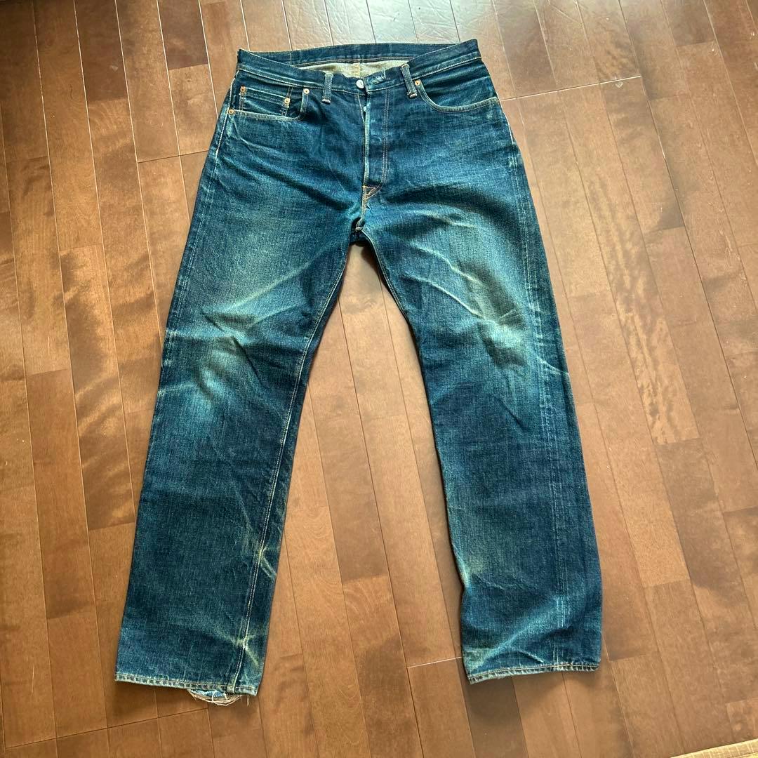 Front view of men's DENIME Lot 016 jeans (W34) laid flat on a wooden floor showing faded indigo denim and front pockets.