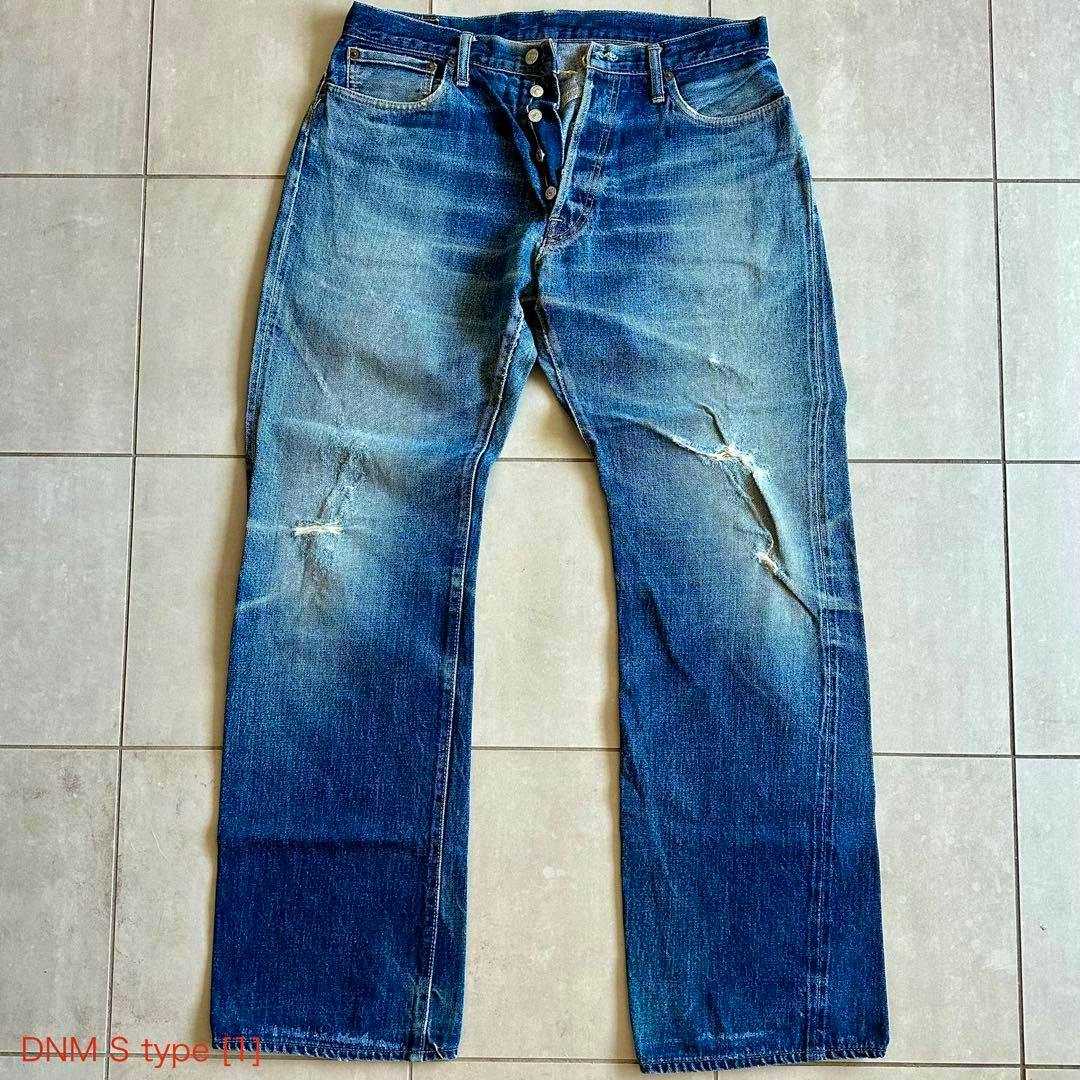 Front view of a pair of men's 34-inch denim jeans laid flat showing a button fly and distressed knees.