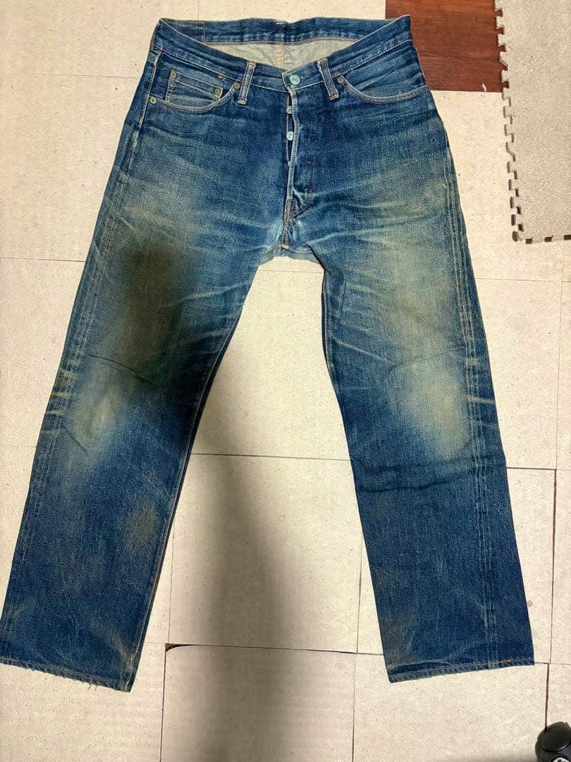 Front view of indigo men's jeans laid flat on the floor showing faded areas and visible button closure.
