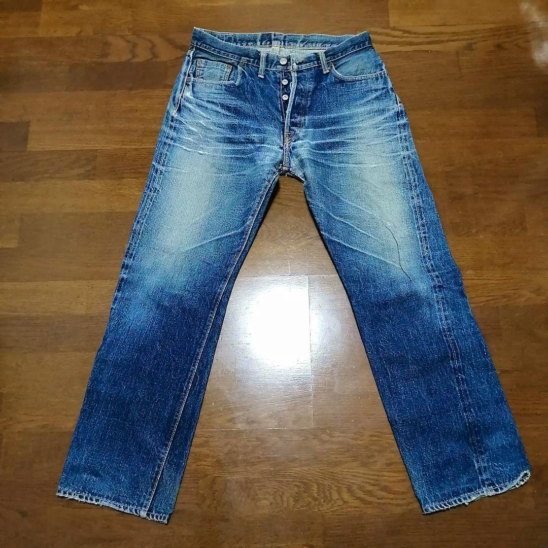 Front view of men's blue Denime denim jeans laid flat on a wooden floor.