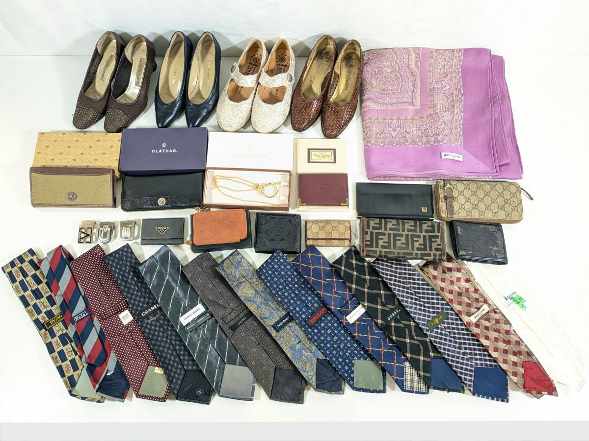 Wide flat-lay photo of a bulk set of branded small items: several pairs of shoes, wallets, a scarf, and many neckties arranged on a white surface.
