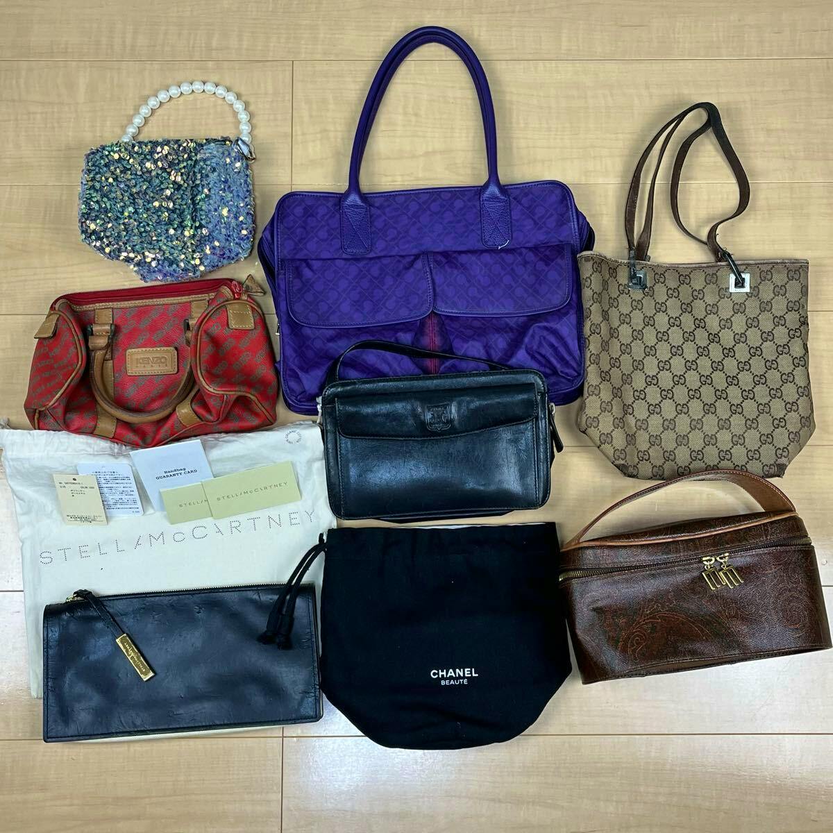 Overhead photo of eight assorted branded bags and dustbags laid flat on a wooden floor, including a Gucci monogram tote.