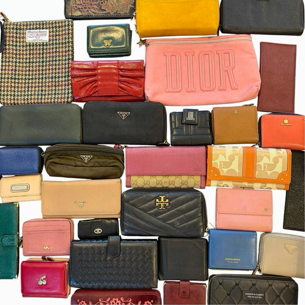 Top-down photo showing many wallets and small pouches from various brands (visible Dior, Prada, Gucci) arranged on a white background.