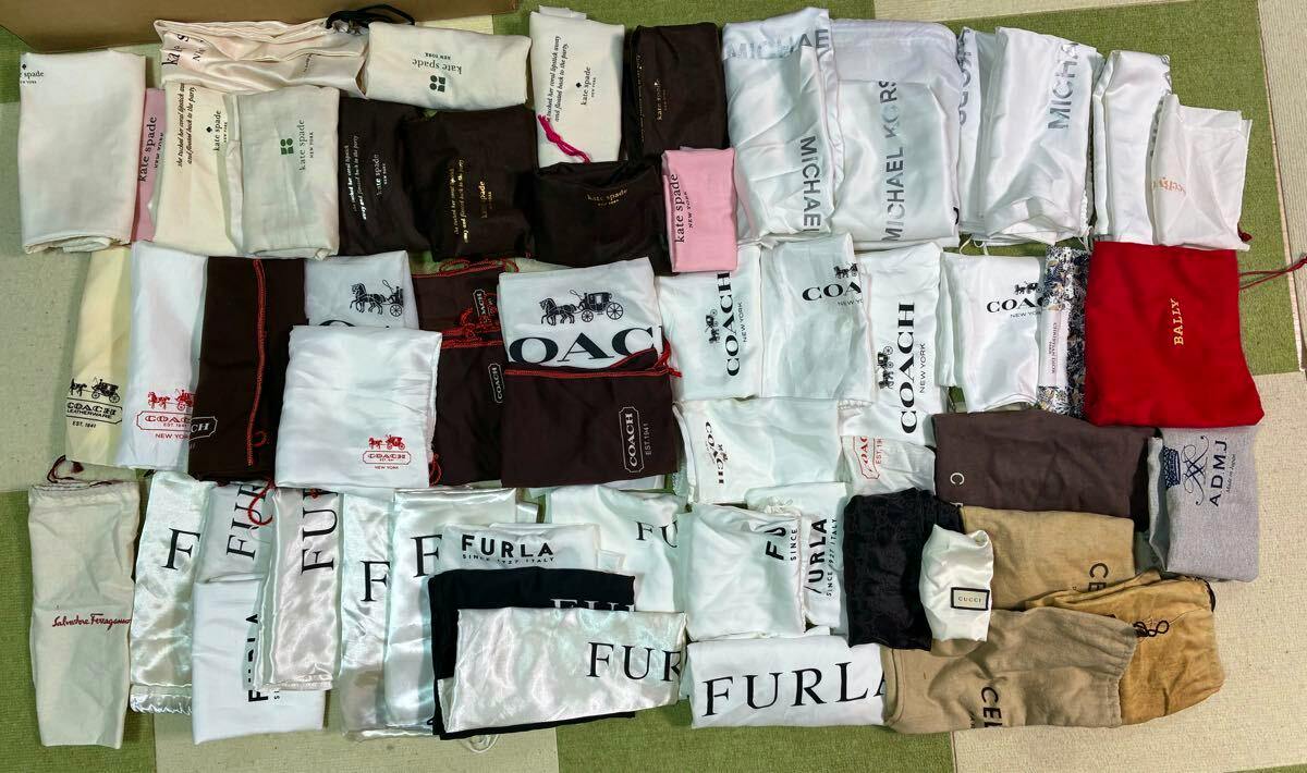 A large assortment of branded cloth storage/dust bags laid flat, showing logos such as Coach, Furla, and Michael Kors.