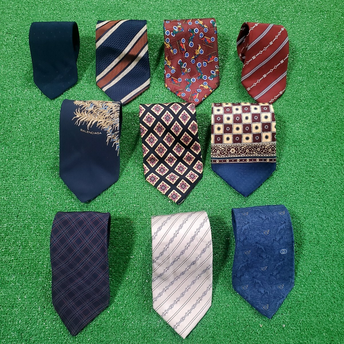Ten neckties laid out on a green surface.