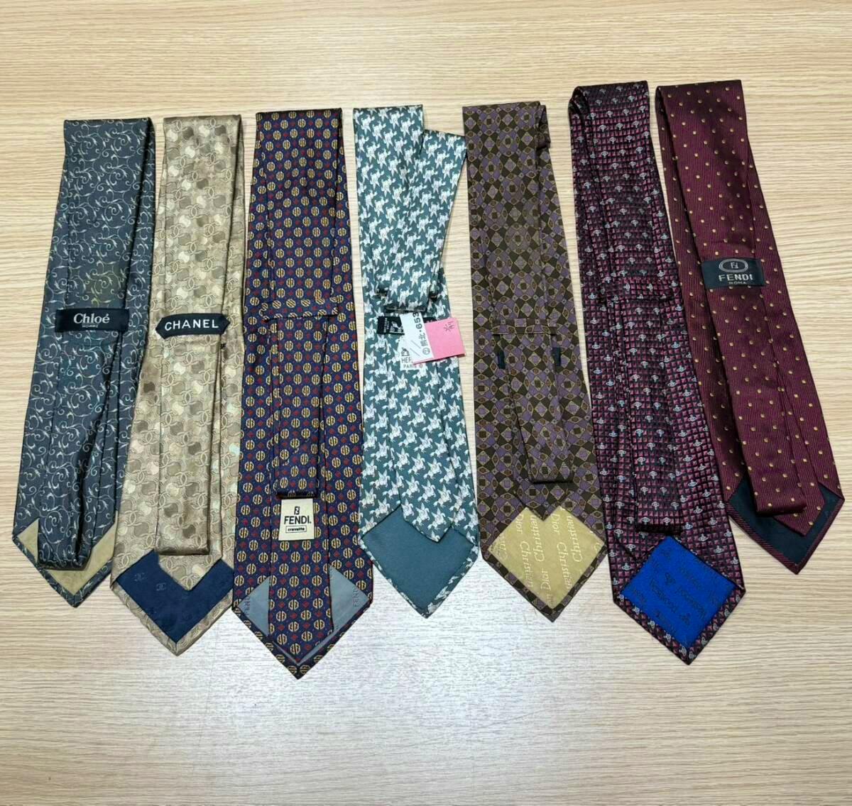 Seven silk neckties from a luxury-brand bundle (Chanel, Fendi, Chloé, Christian Dior, Vivienne Westwood, Hermès) laid flat on a wood surface.