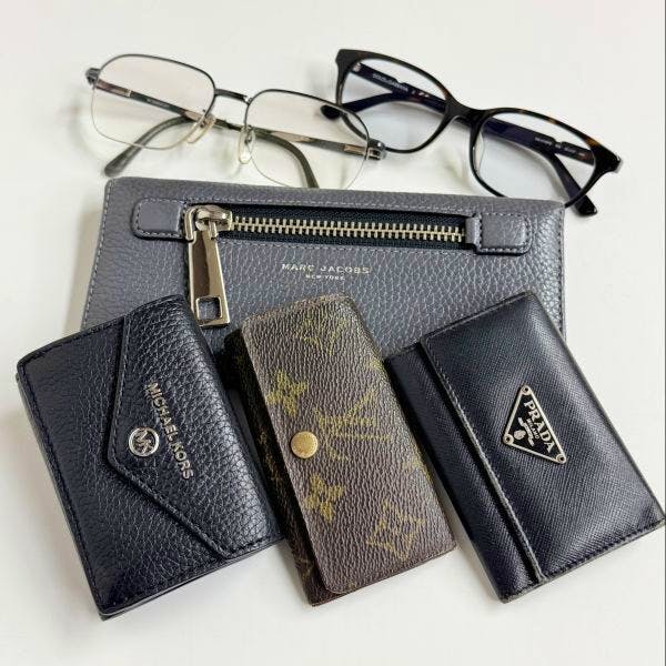 Several small wallets and key cases, a zip pouch, and two pairs of eyeglasses arranged on a white background.