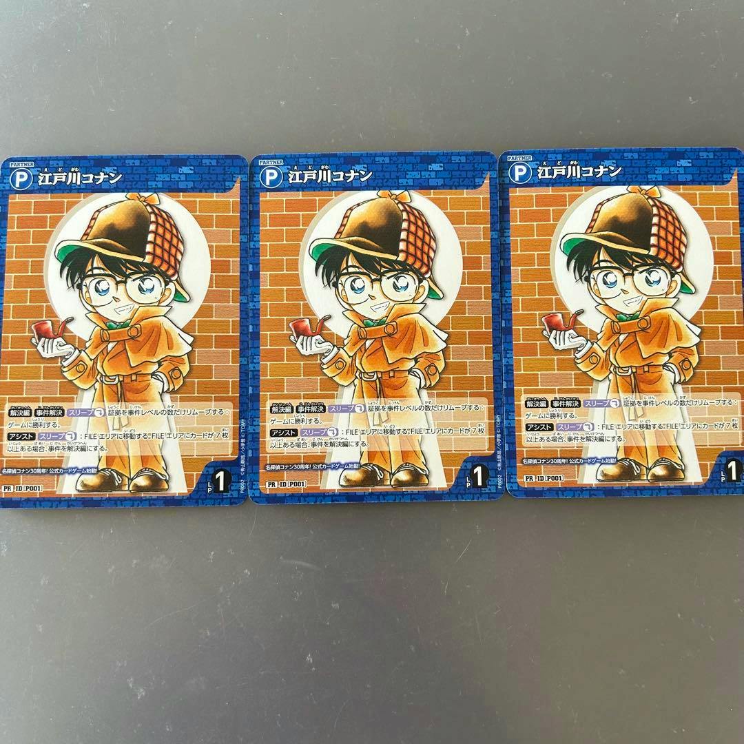 Three promotional Detective Conan trading cards showing Edogawa Conan in a detective outfit arranged side-by-side on a gray surface.