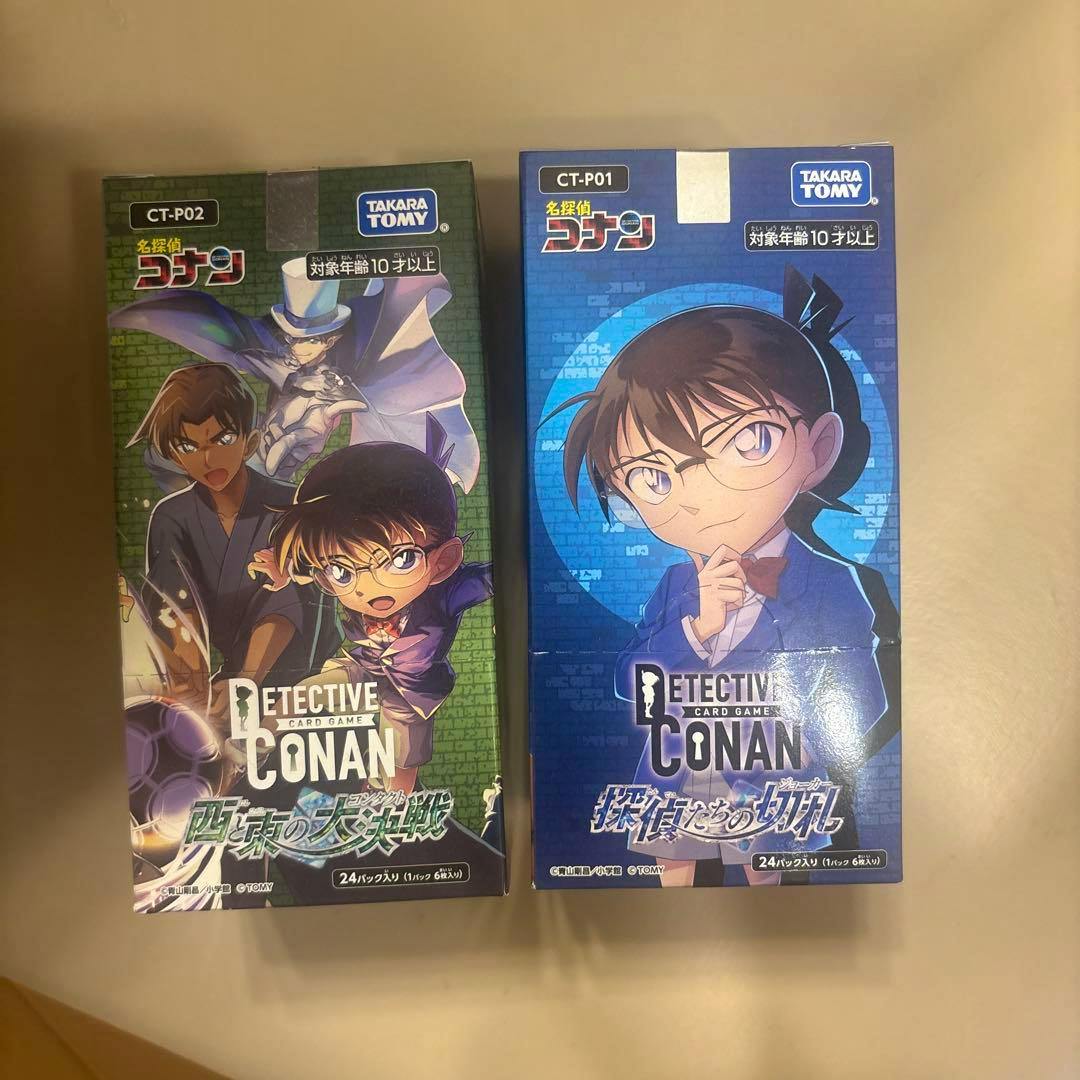 Photo of two boxed Detective Conan trading card game boxes side by side, the left box with green artwork and the right box with blue artwork.
