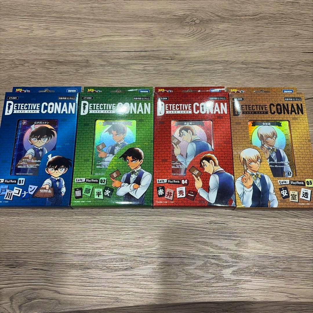 Four Detective Conan card game start deck boxes (blue, green, red, orange) arranged side by side on a wooden surface.