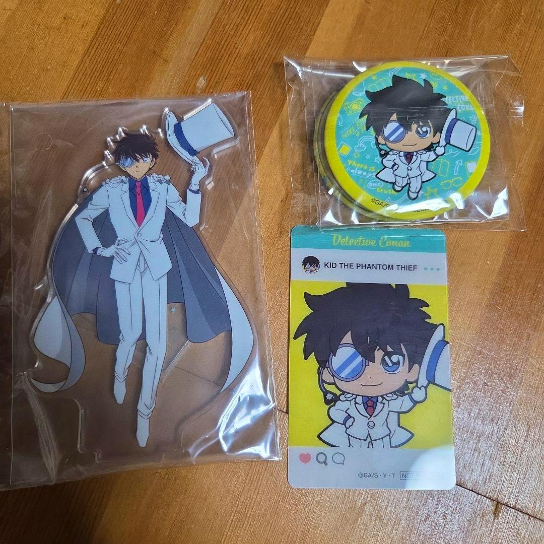 A set of Detective Conan (Kaitou Kid) goods including an acrylic decorative stand, a round badge, and an illustrated card on a wooden surface.
