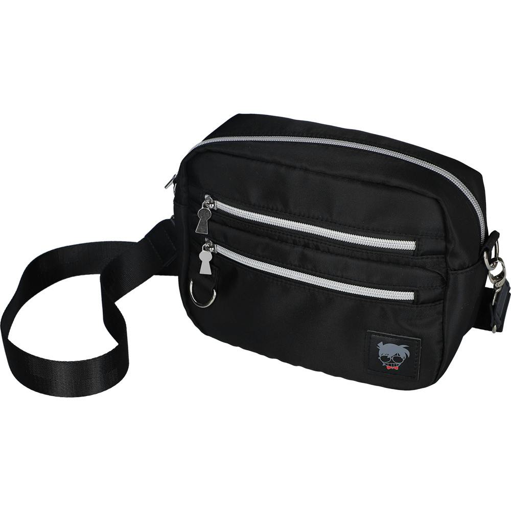 Front view of a black polyester shoulder bag with silver zippers, two front zip pockets, a key ring, and a small character patch on the lower corner.