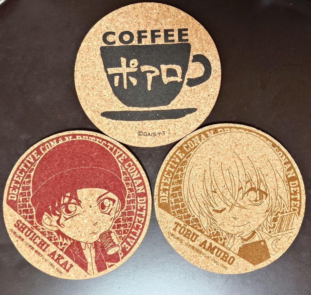 Three round cork coasters on a dark surface: two printed with character portraits labeled "SHUICHI AKAI" and "TORU AMURO", and one printed with a coffee cup and the word "COFFEE".