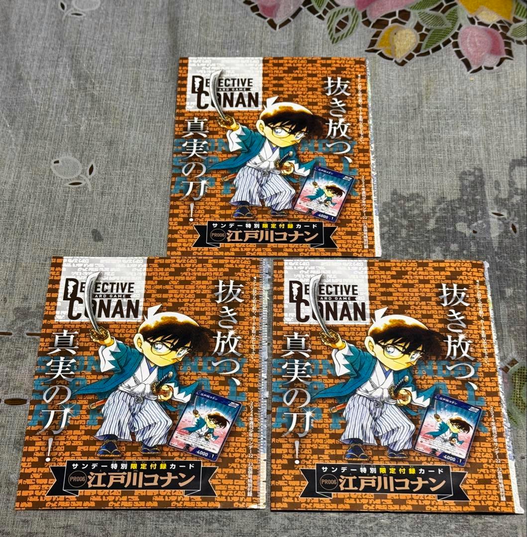 Three sealed Detective Conan trading-card promotional sheets showing Conan in a Shinsengumi-style outfit laid out on a fabric surface.