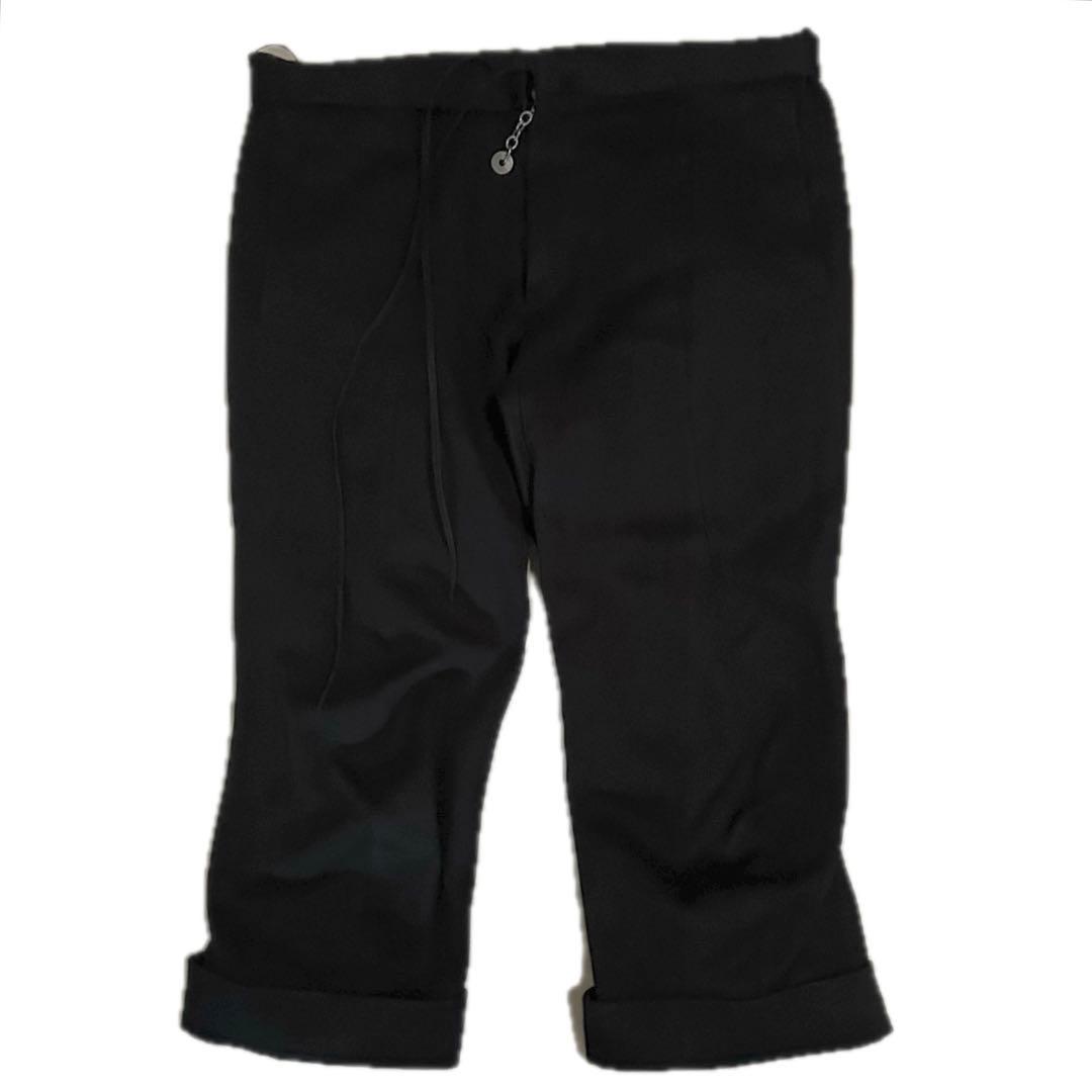 Front view of black cropped men's cotton pants with rolled cuffs and a coin charm at the waistband.
