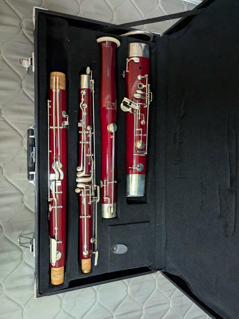 Four disassembled bassoon sections placed in a black foam-lined carrying case on a quilted surface.