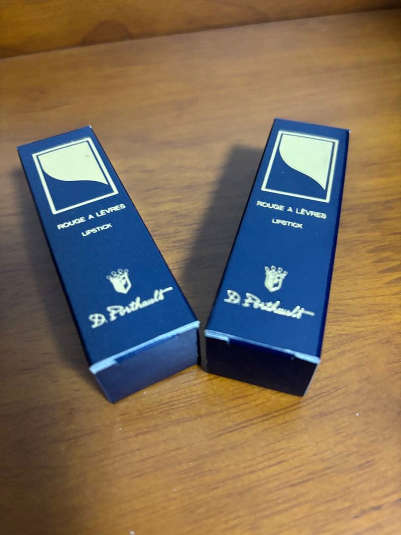 Two boxed lipsticks placed on a wooden surface.