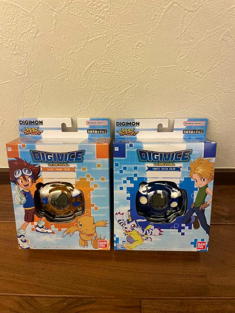 Two boxed Digimon Digivice Ver.REVIVAL toys shown side-by-side on a wooden floor against a wall.