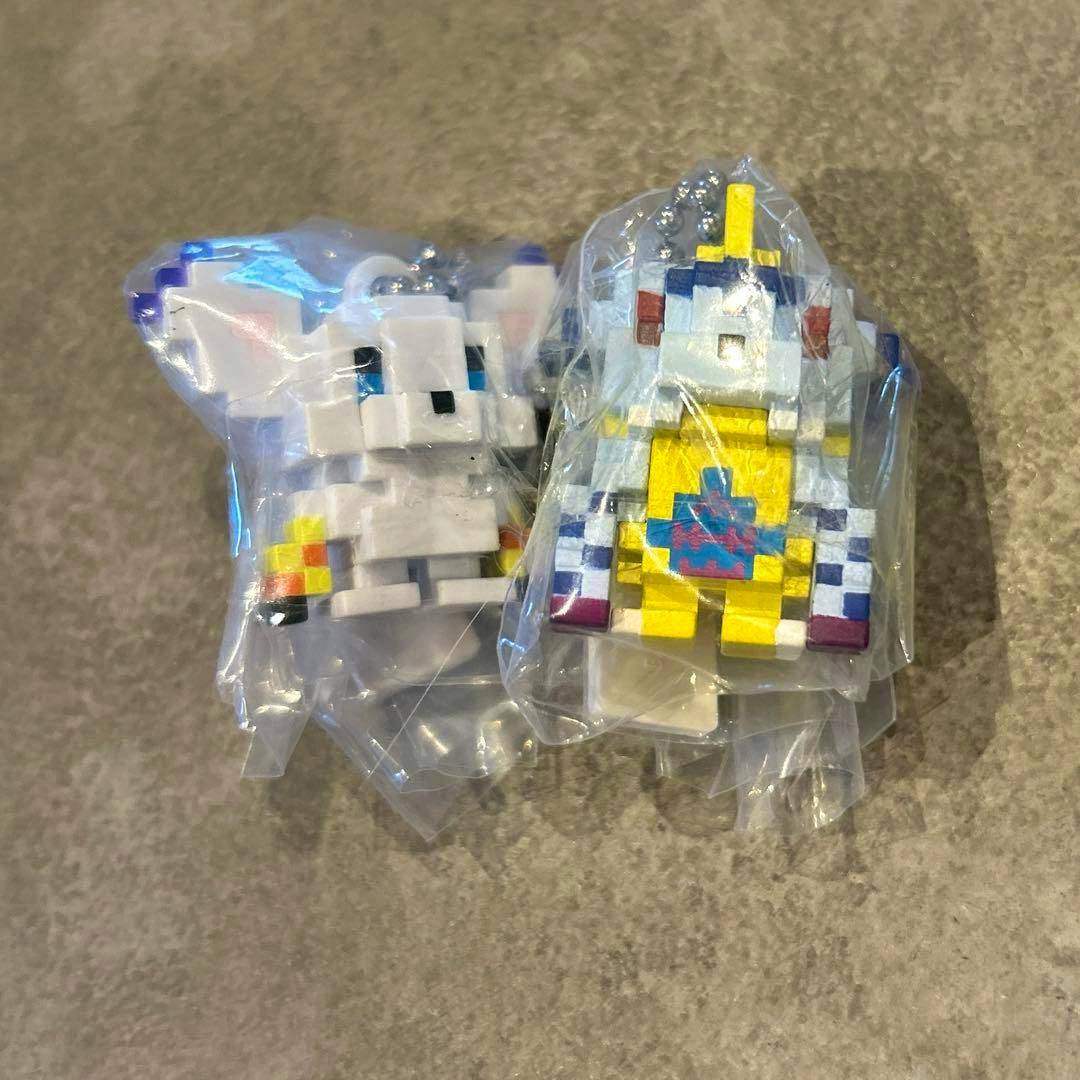 Two Digimon dot-style plastic figure charms sealed in clear plastic bags on a gray surface.