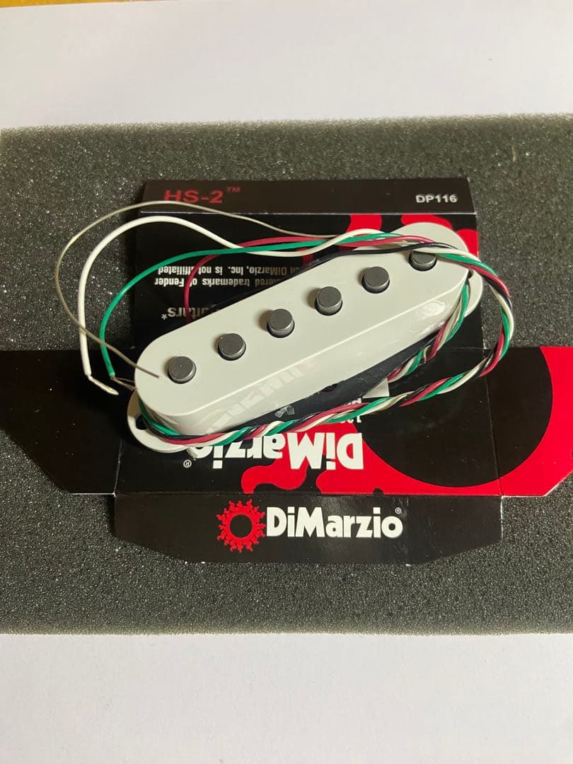 White DiMarzio HS-2 guitar pickup with attached wires resting on DiMarzio packaging and foam.