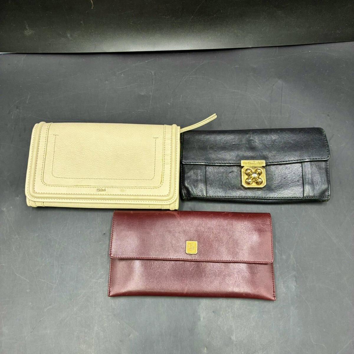 Three long leather wallets (white, black, and burgundy) arranged on a dark surface.