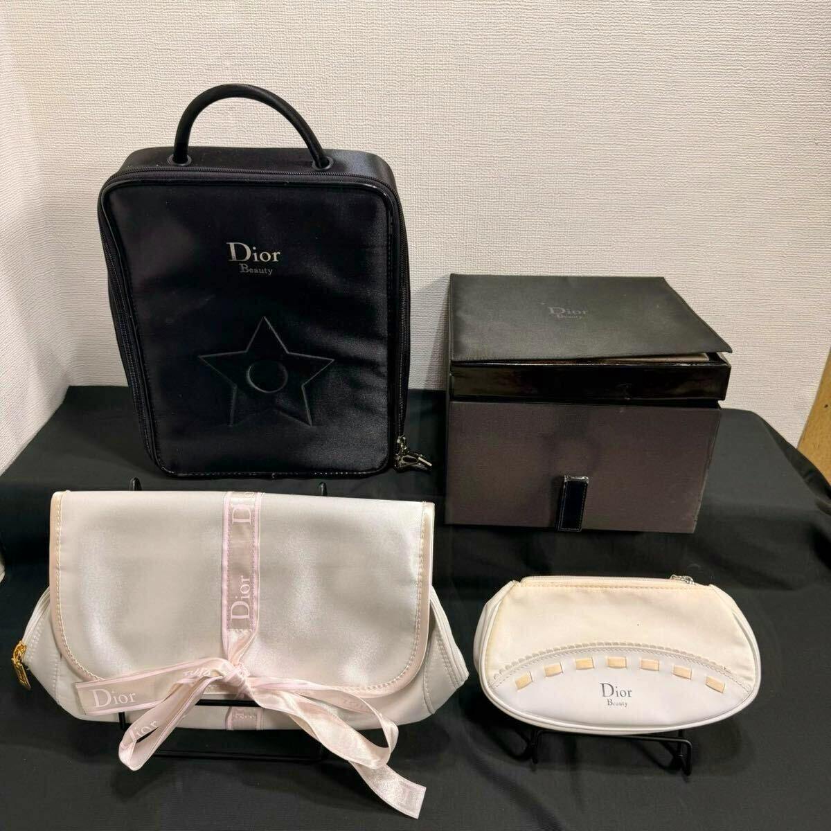 Black Dior Beauty box-bag, a storage box, and two white Dior cosmetic pouches displayed on a black surface.