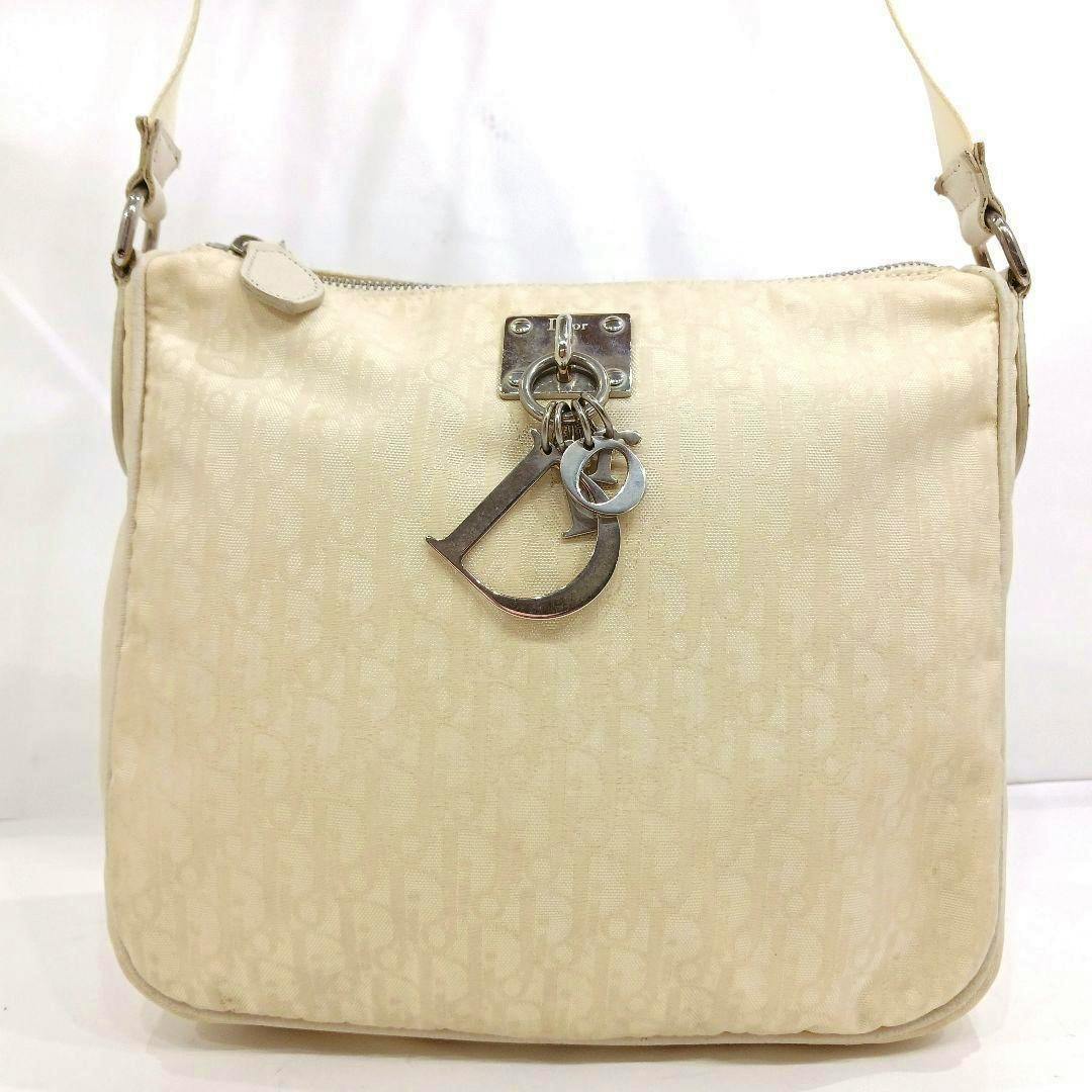 Front view of a white Dior shoulder bag in trotter-pattern canvas with dangling metal "D" charms.