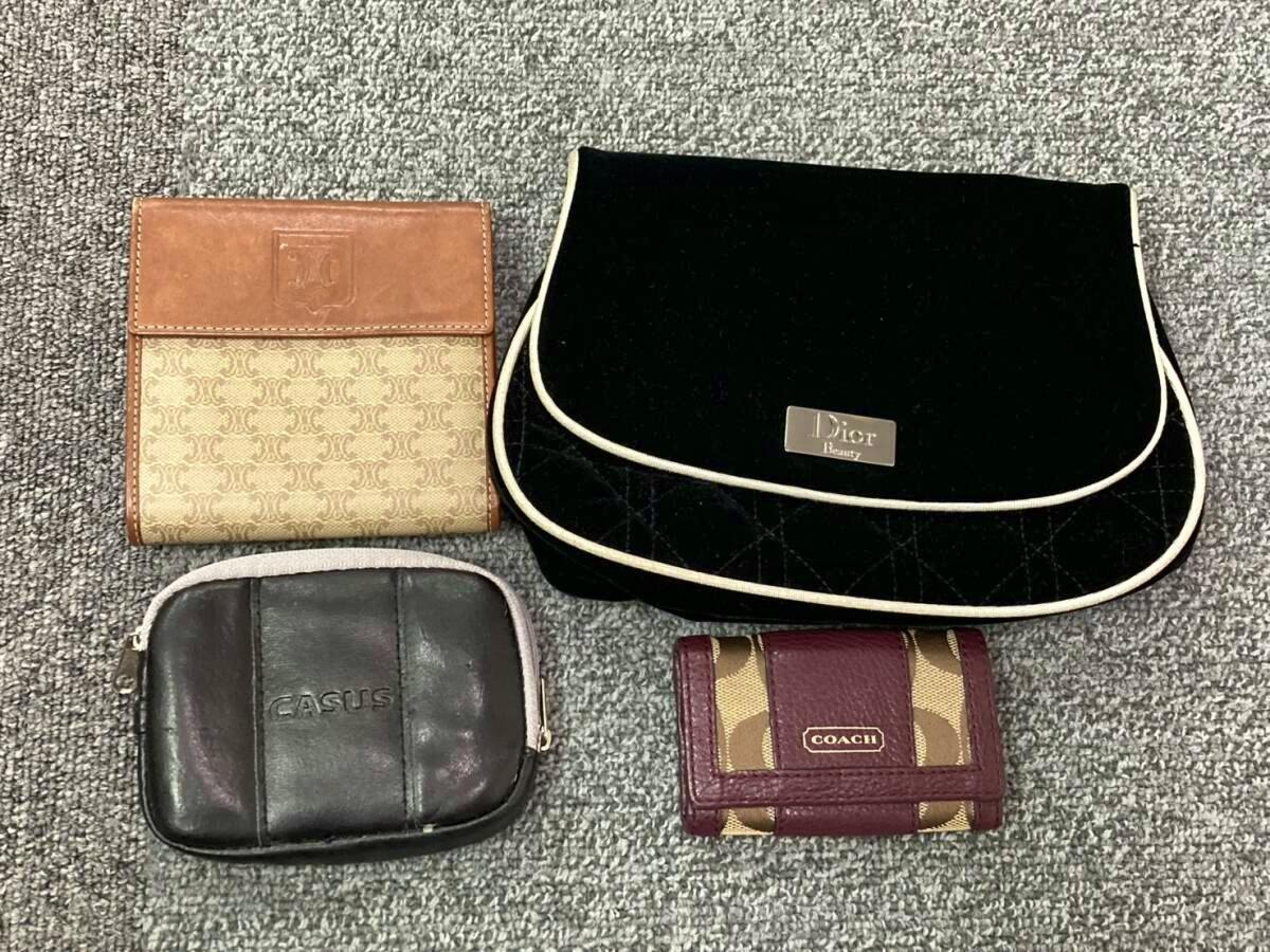 Four small wallets and pouches laid on carpet, including a Dior pouch, a Coach wallet, a brown patterned wallet, and a small black CASUS pouch.