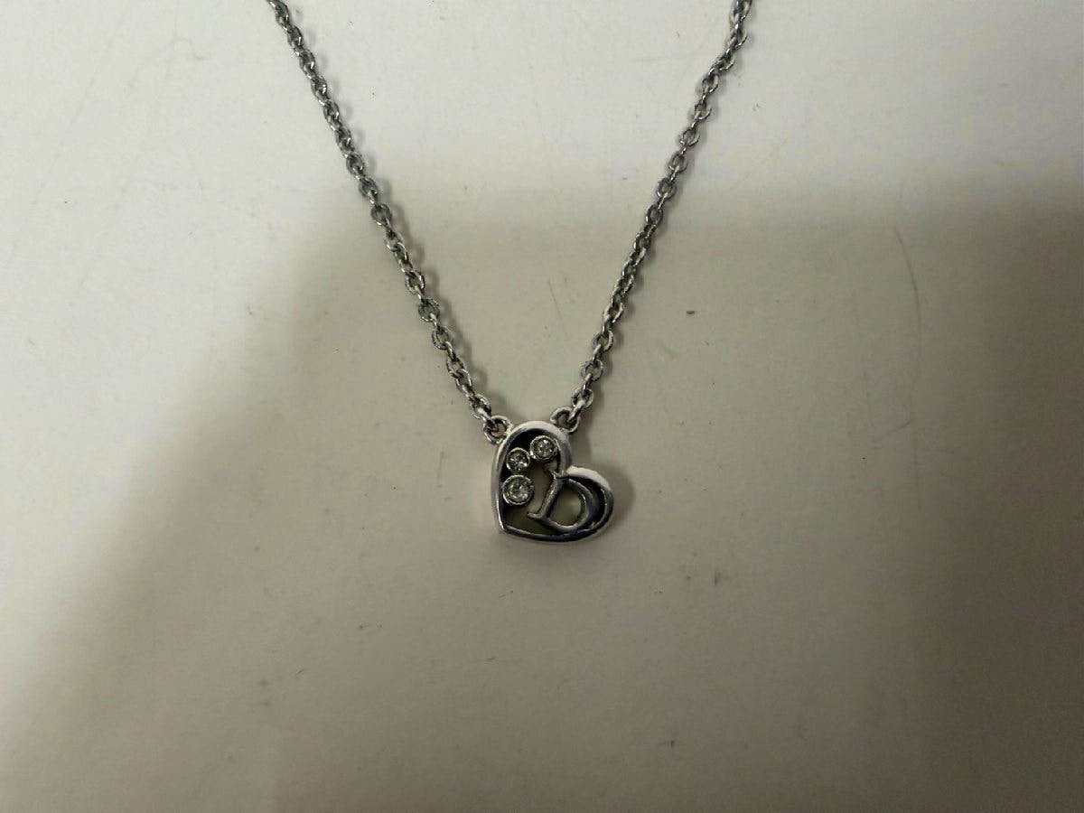 Metal necklace with a heart-shaped pendant featuring a D logo and three small rhinestones on a chain against a white background.