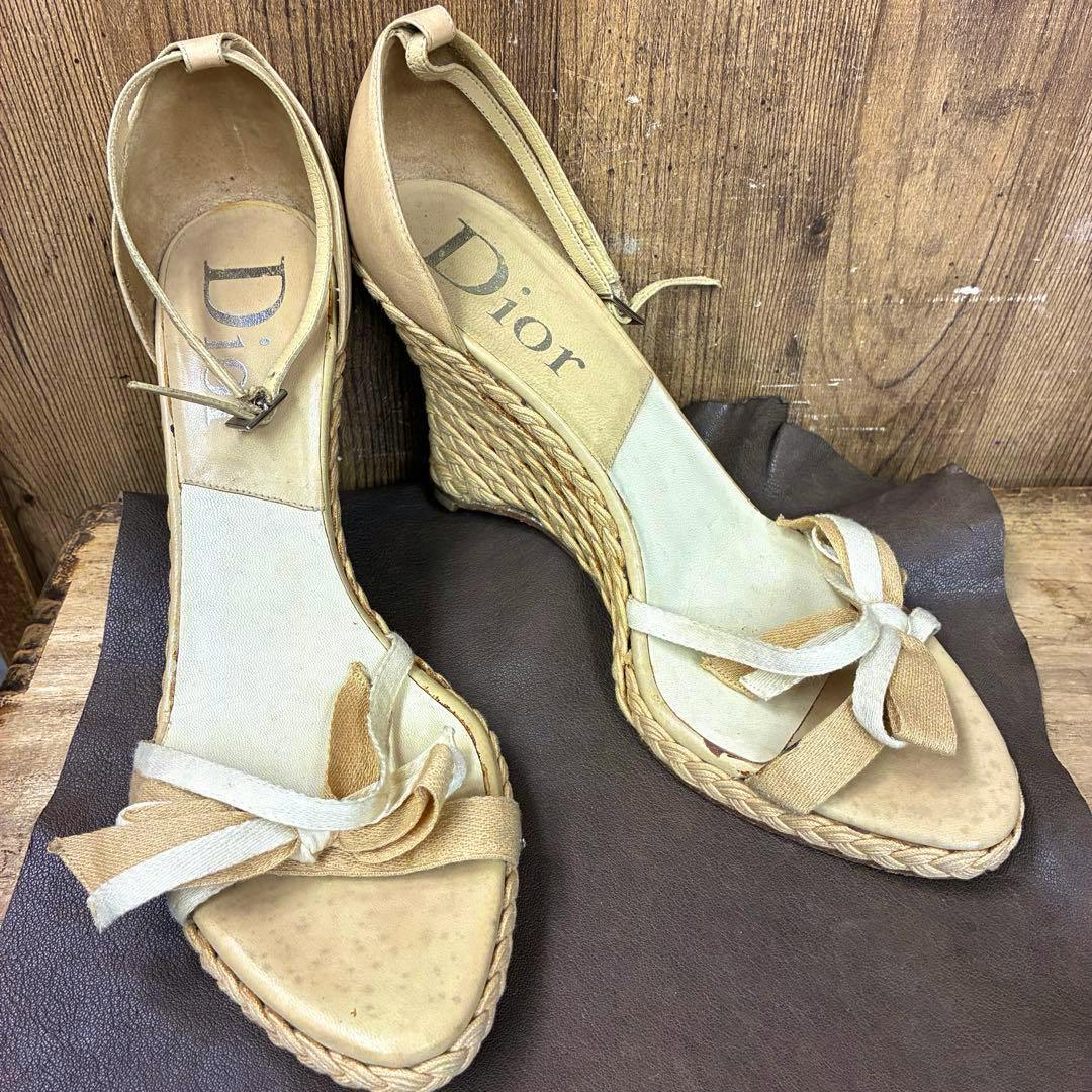 Overhead photo of a pair of beige Dior high-heel sandals with ankle straps, woven wedge heels, and front bow details.