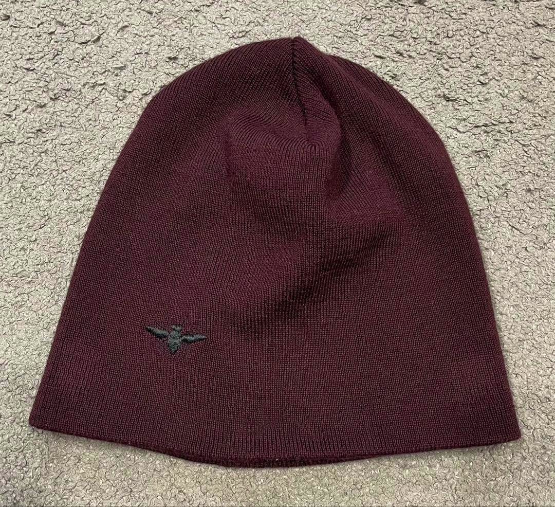 Maroon knit hat laid flat showing a small embroidered bee detail on the front.