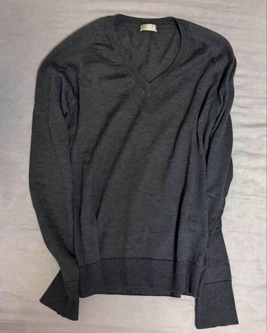 Dark V-neck wool sweater laid flat showing the front of the garment with ribbed cuffs and hem and the neck label visible.