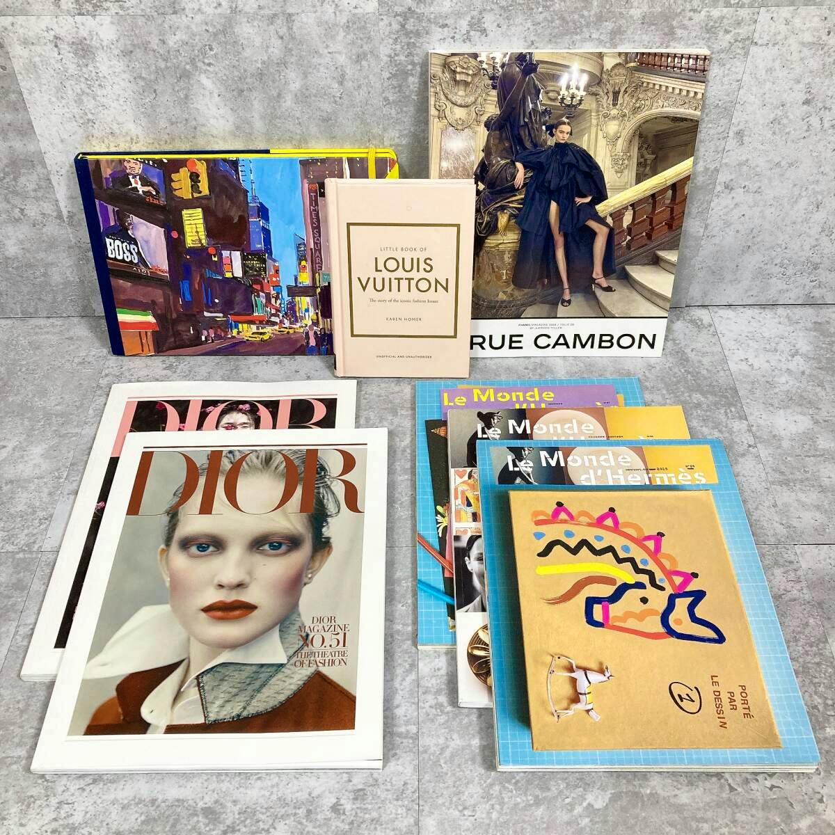 Photo of a collection of brand magazines and booklets including Dior, Louis Vuitton, Rue Cambon, and assorted Le Monde d'Hermès issues arranged on a floor.