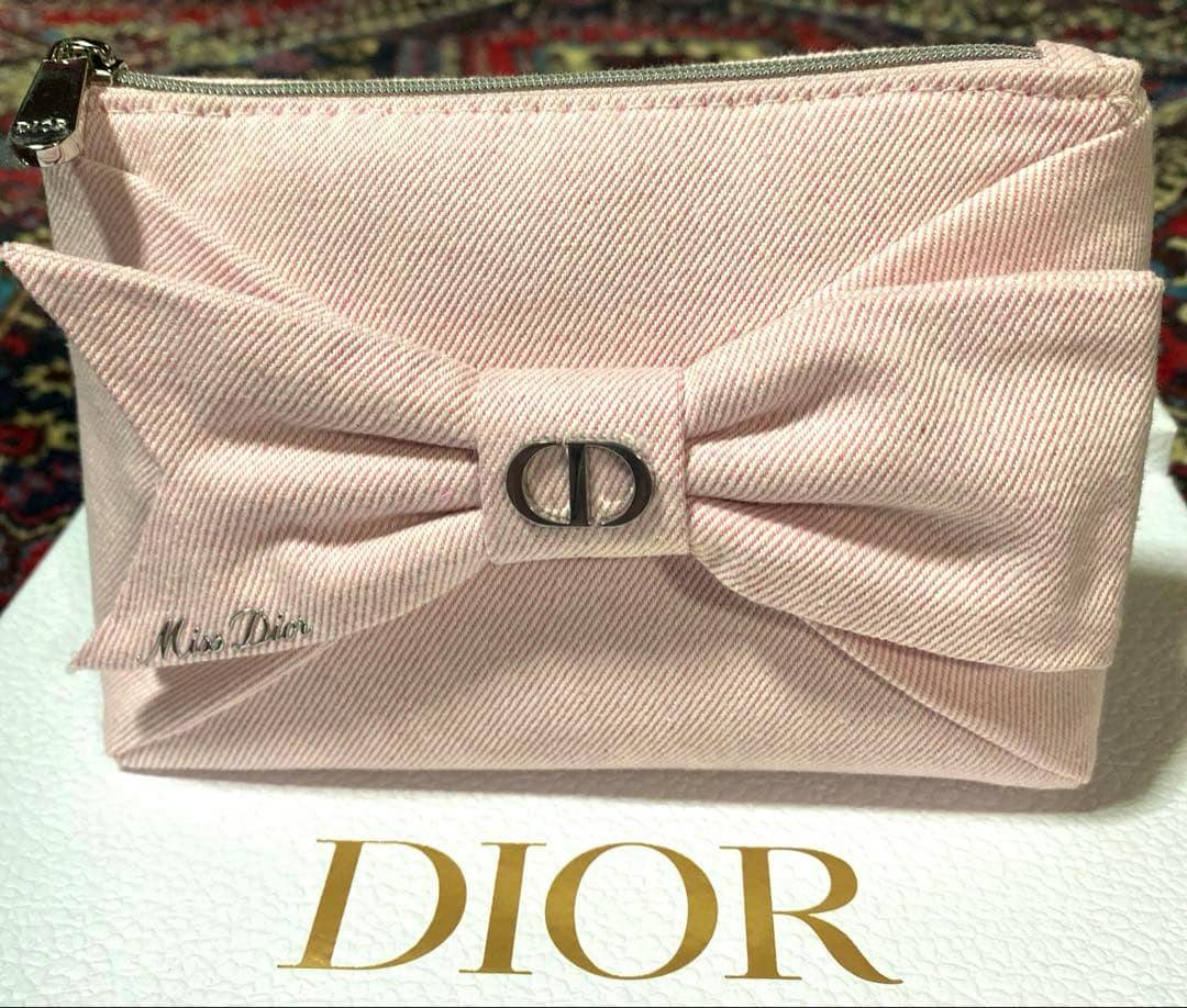 Light pink Miss Dior pouch with a bow and CD metal logo sitting on a white surface showing gold DIOR text.