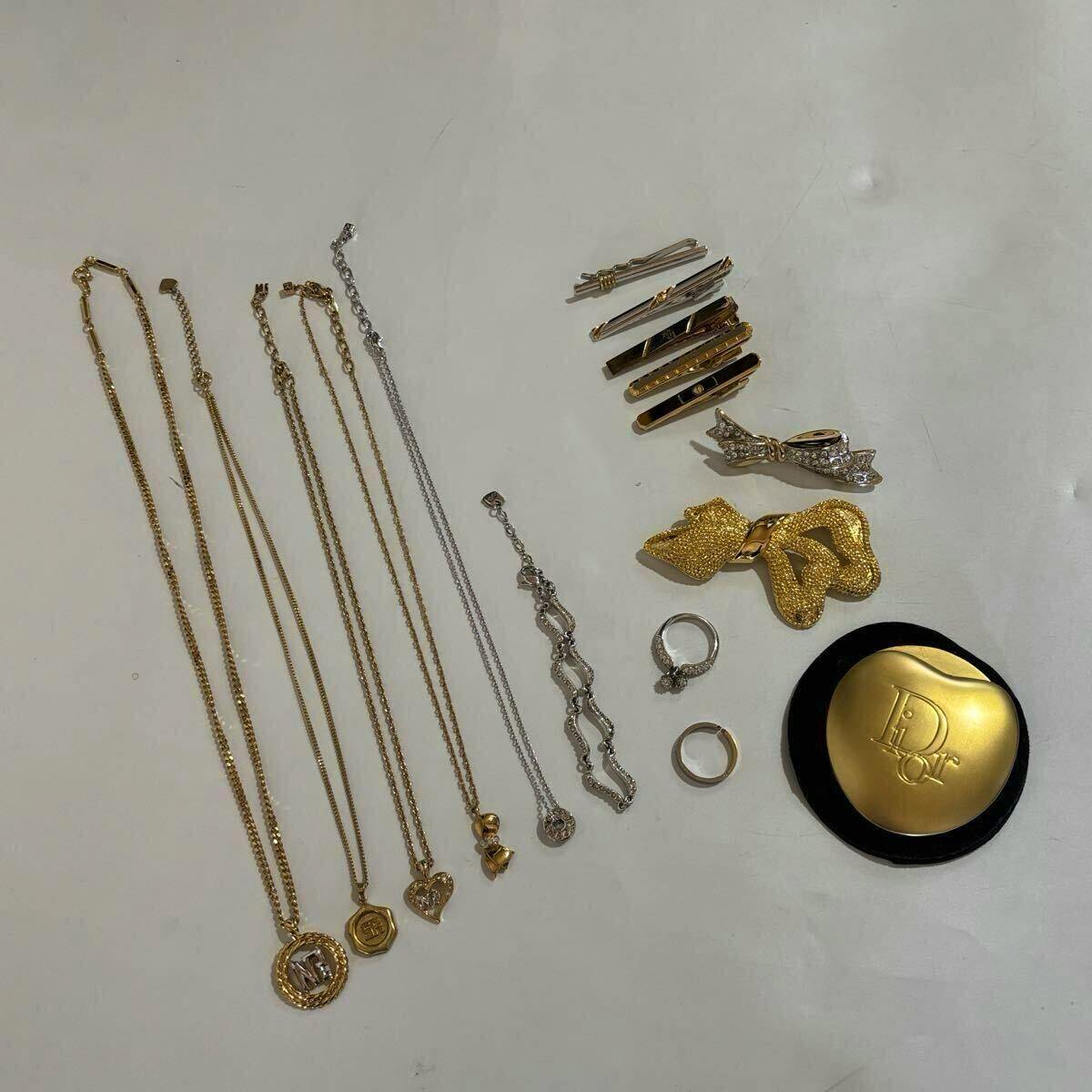 Multiple gold and silver necklaces and assorted costume-jewelry items including rings, brooches, hair clips, and a gold compact arranged on a white surface.
