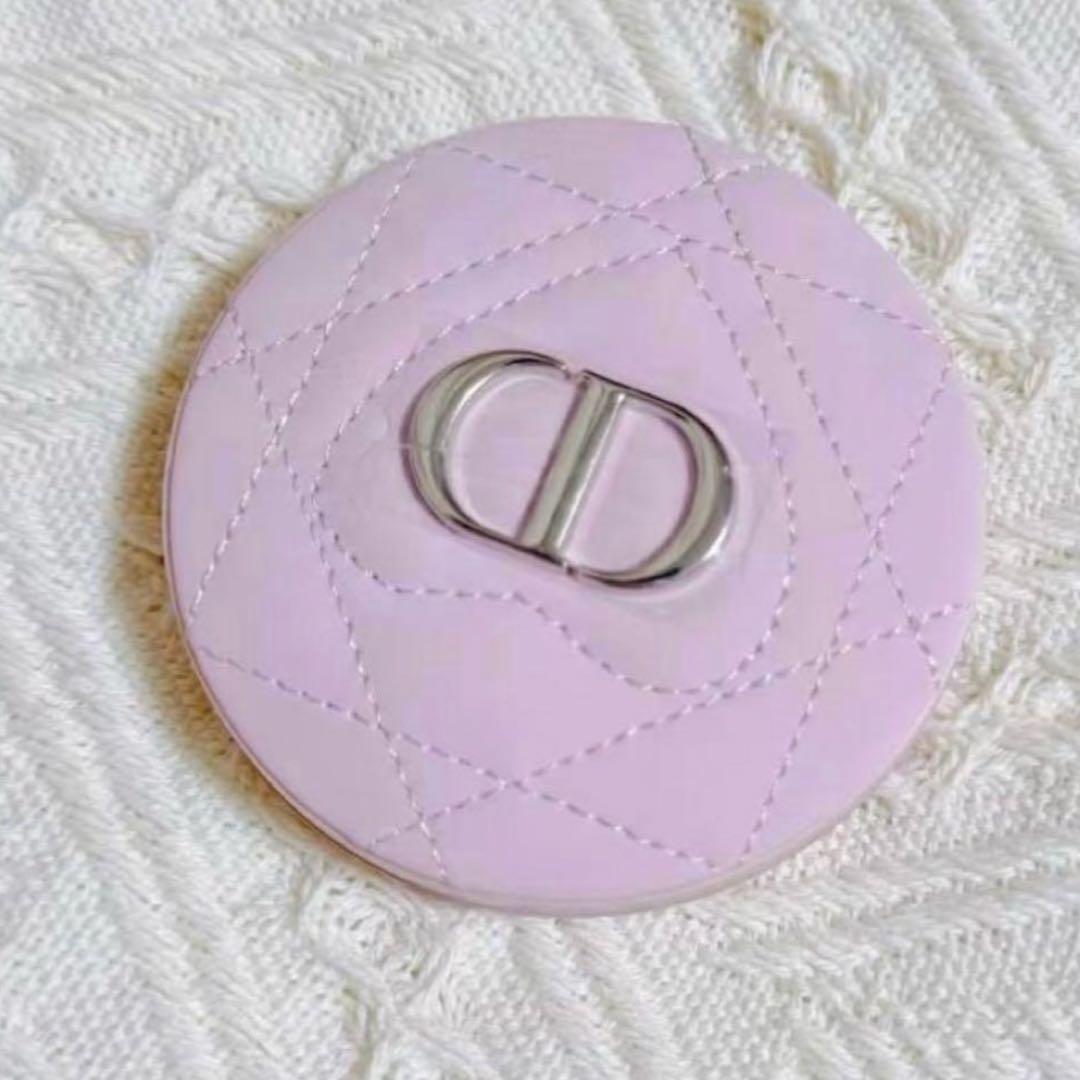 Pink Dior compact mirror with quilted stitching and metal CD logo shown closed on a knit background.