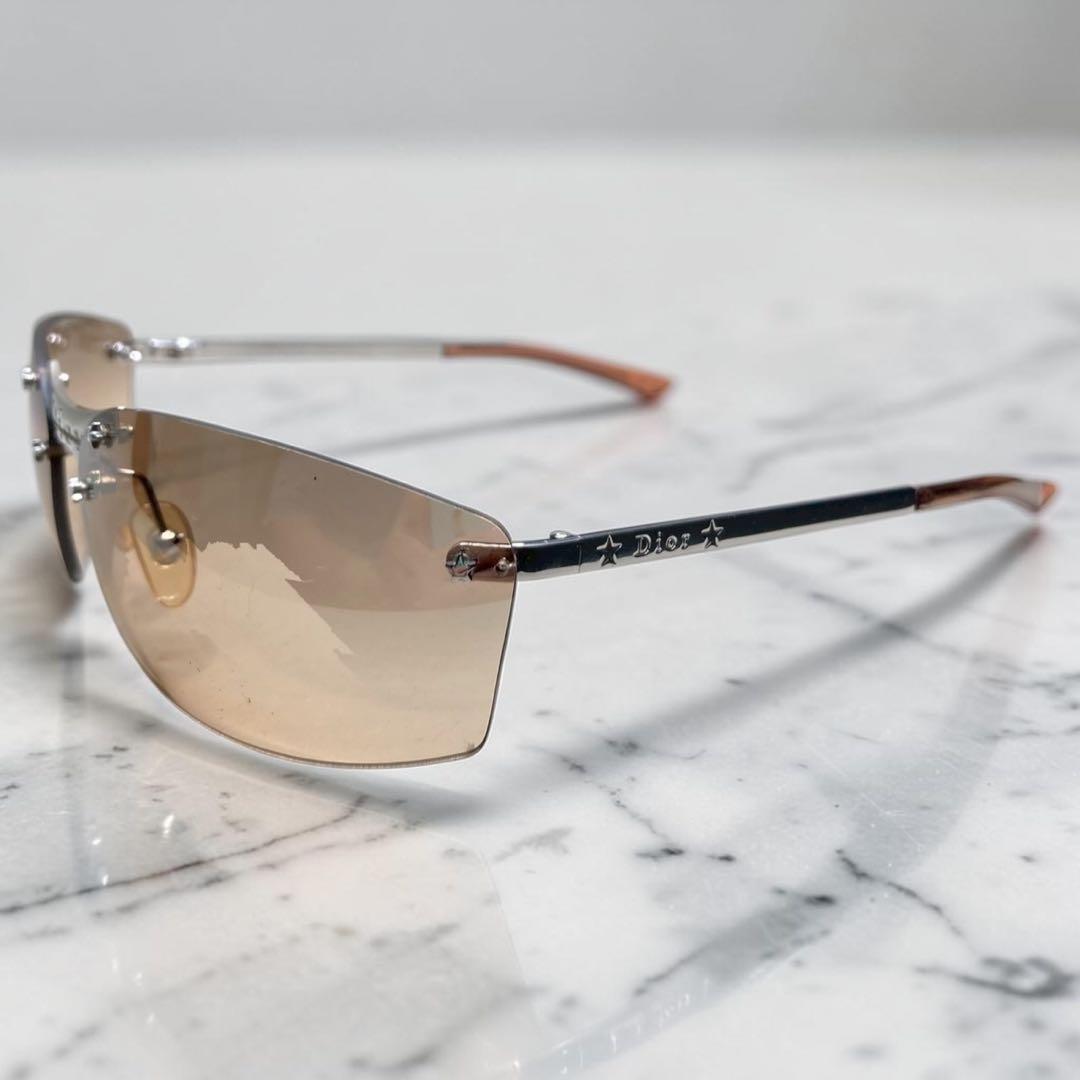 Rimless Dior sunglasses with brown-tinted lenses and silver temples showing the Dior logo, photographed on a marble surface.