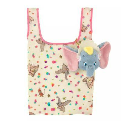 A cream-colored shopping bag printed with repeating Dumbo illustrations and colorful dots, with an attached Dumbo plush pouch.